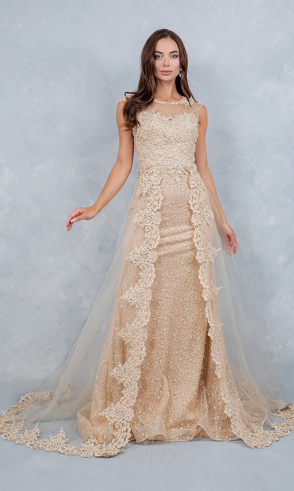 A woman stands posing against a light gray textured background, wearing the Cinderella Couture 8506J long formal dress in champagne—a sleeveless, floor-length gown featuring lace appliques and a sheer tulle fabric overlay.